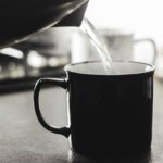 Uomo che beve un bicchiere d'acqua calda al mattino, con focus su salute e benessere.